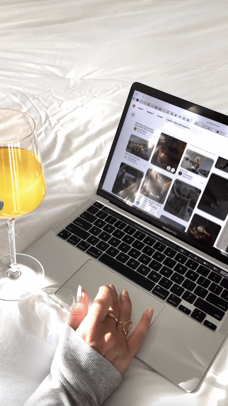 A hand on a laptop touchpad next to a glass of orange juice on a white bedspread, researching how to start an anonymous blog for free.