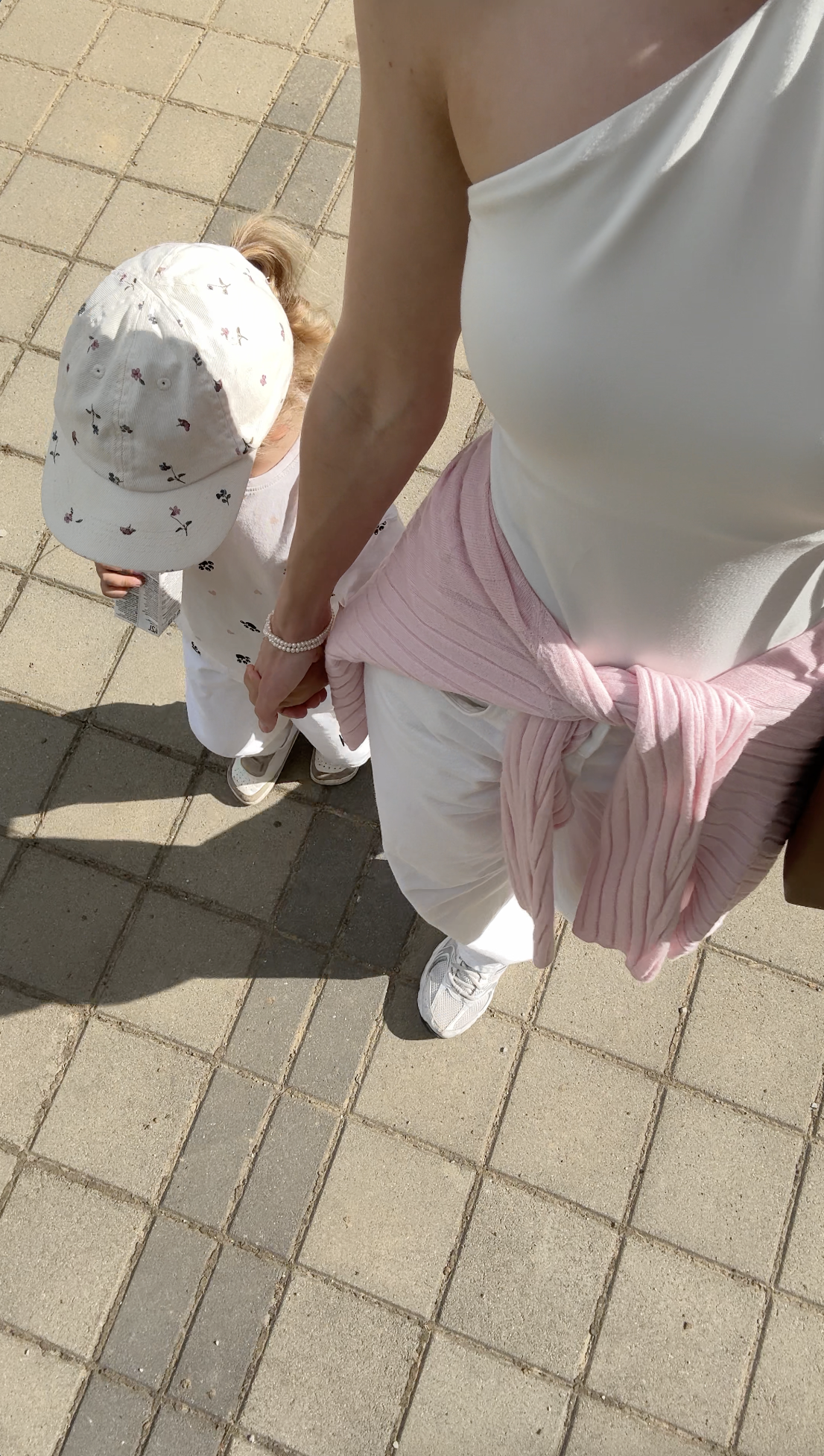 Woman holding a childs hand while walking on a paved path, both dressed in white and pink—an image that beautifully captures connection, perfect for illustrating concepts like What Is Faceless Marketing through anonymous yet relatable visuals.