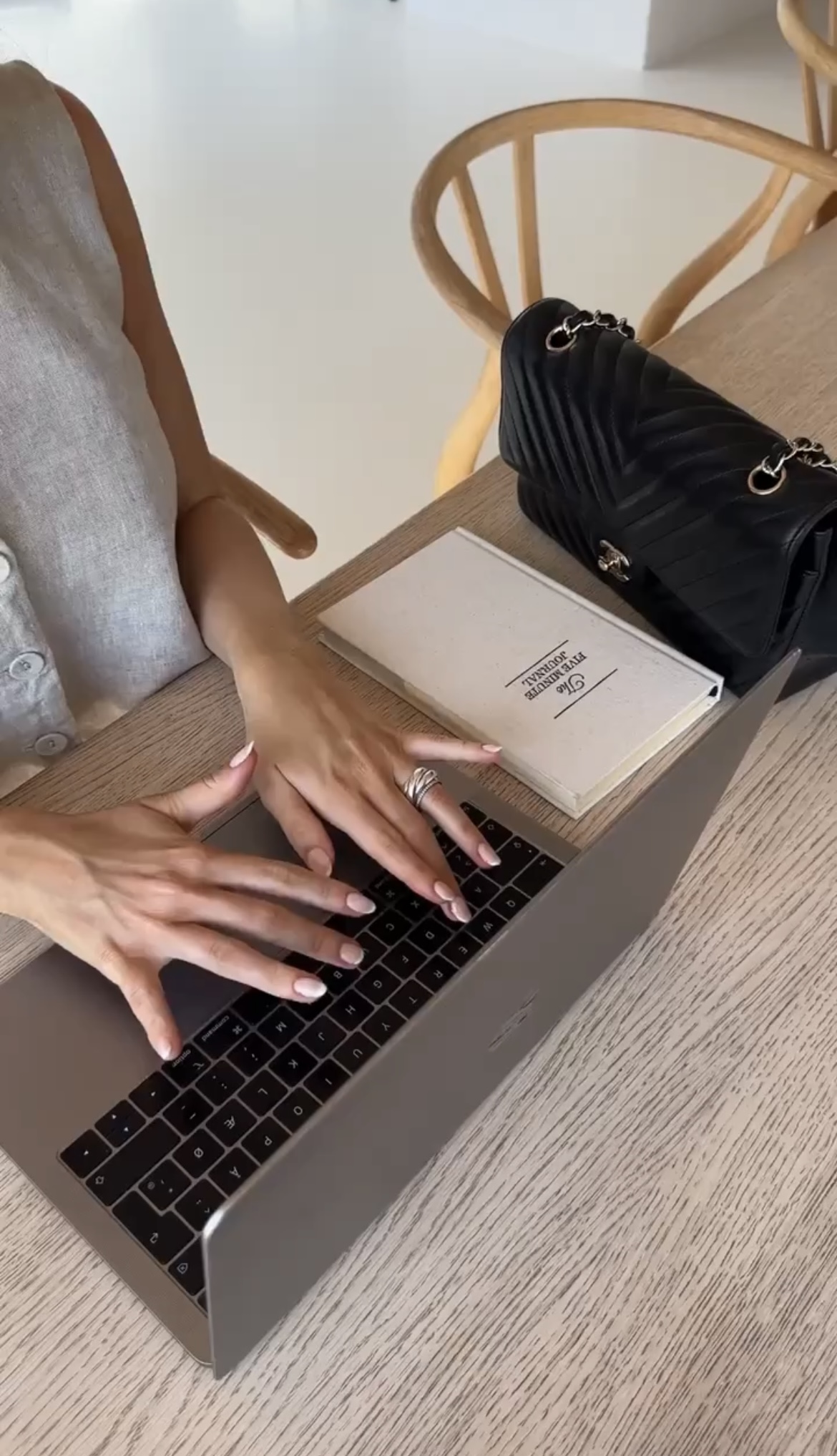 A person typing on a laptop at a wooden table with a notebook and black handbag nearby, researching the easiest Faceless Business ideas.