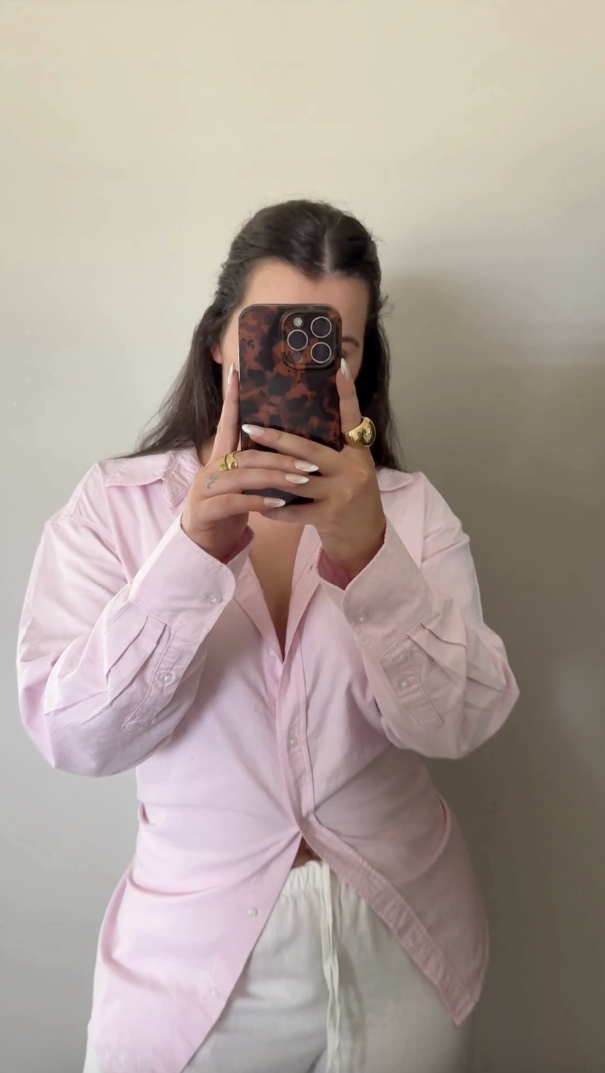 Person in a light pink shirt takes a mirror selfie with a phone, partially covering their face—a subtle nod to What Is Faceless Marketing.