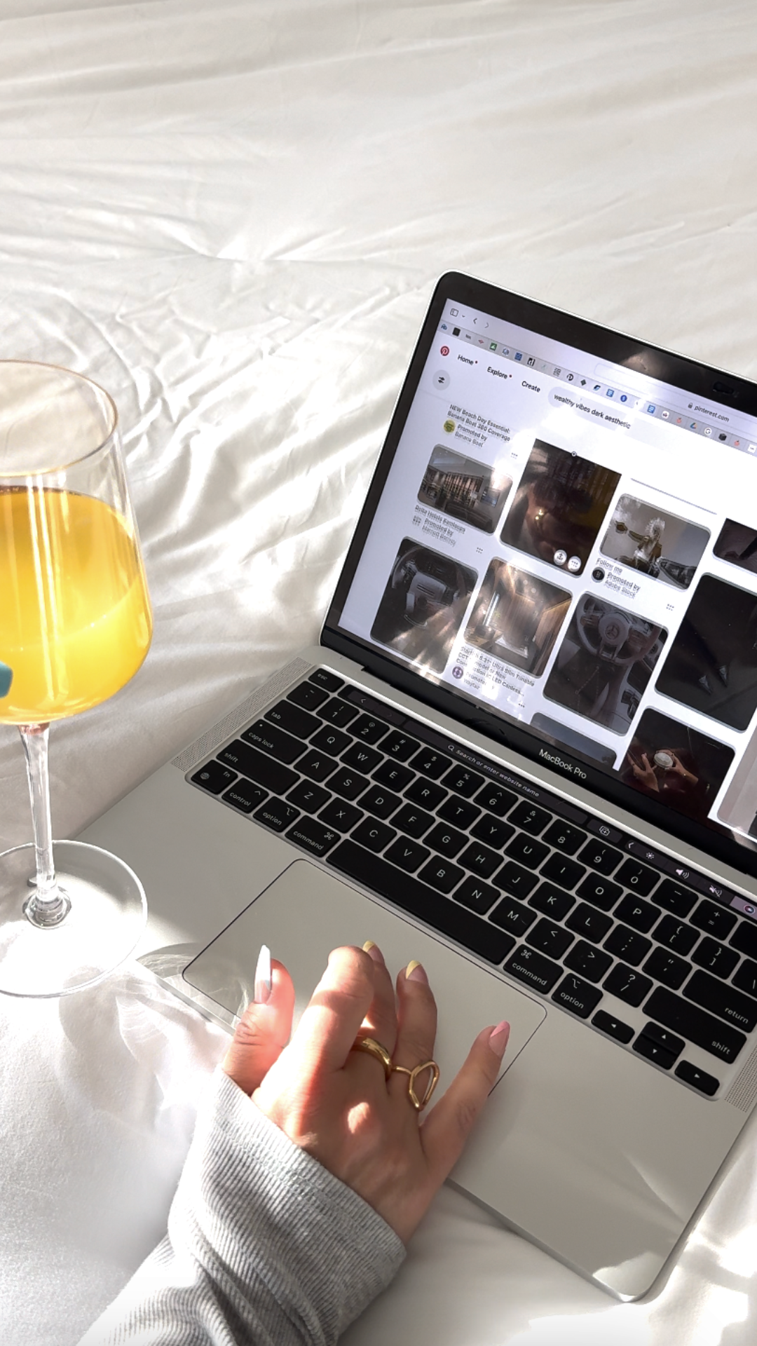 A hand on a laptop trackpad next to a glass of orange juice on a white bed, researching what is faceless marketing.