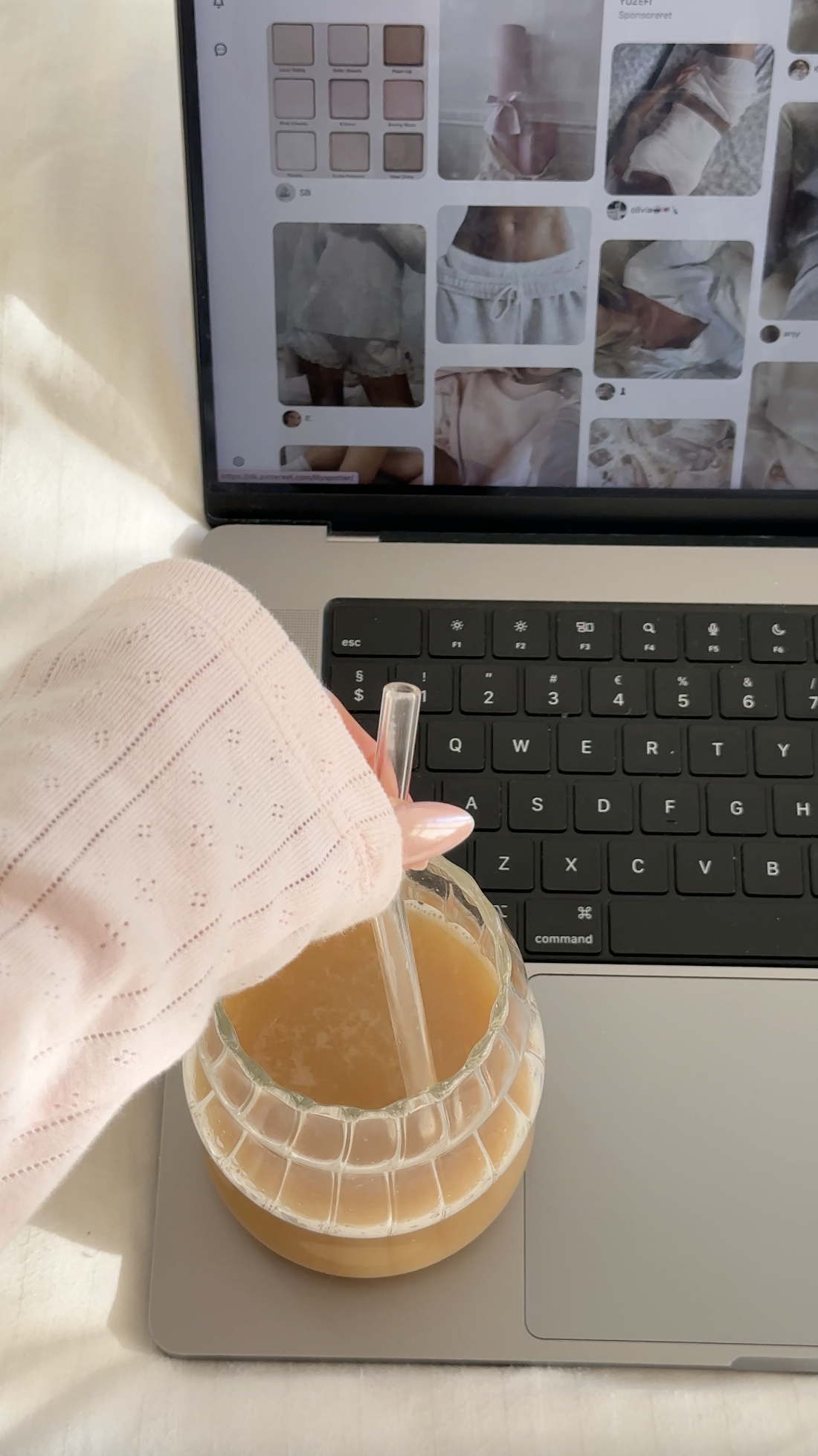 A hand stirs a drink in a glass, with a laptop showing clothing images in the background—a perfect scene for Faceless Affiliate Marketing at work.