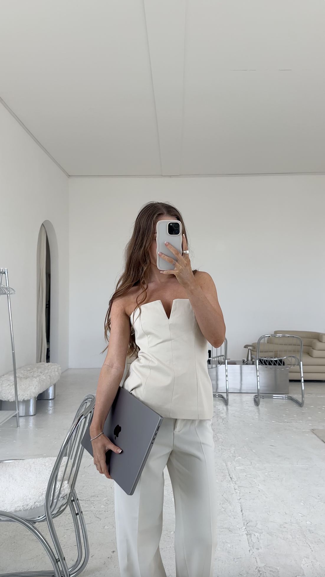 Woman taking a mirror selfie in a white outfit, holding a laptop in a modern, minimalist room—a perfect vibe for passive income and faceless marketing inspiration.