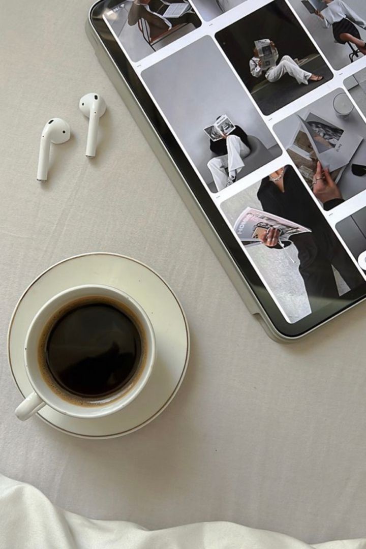 A cup of black coffee, wireless earbuds, and a tablet with photos on a white surface—perfect essentials for planning your next faceless marketing strategy.