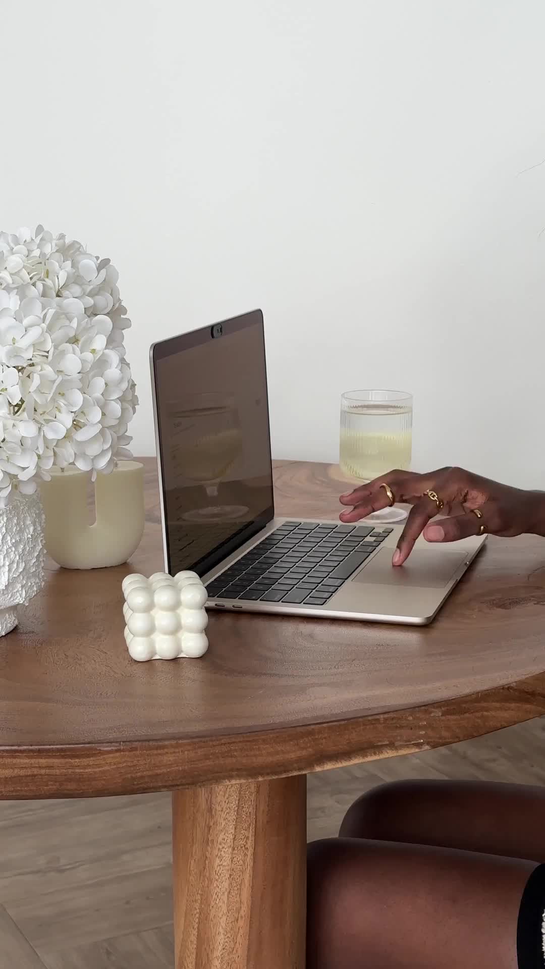A person researching how to start an anonymous blog for free, typing on a laptop at a wooden table with flowers, candles, and a decorative cube nearby.