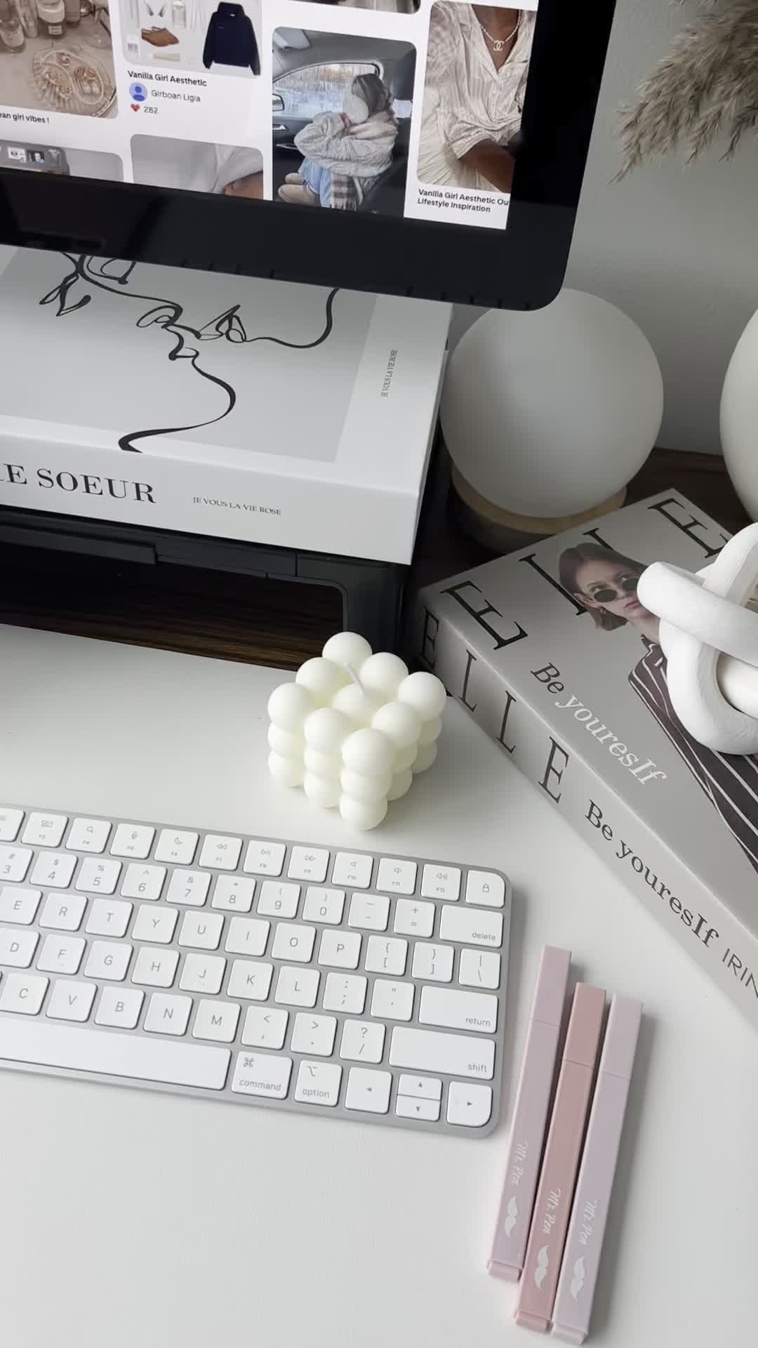 Minimalist desk with a keyboard, bubble candle, books, pink pens, and a computer displaying Pinterest and tips on how to start faceless digital marketing.